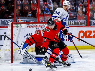 Senators centre Colin White keeps an eye on the loose puck in front of goalie Anton Forsberg and the Maple Leafs' Auston Matthews during the second period.