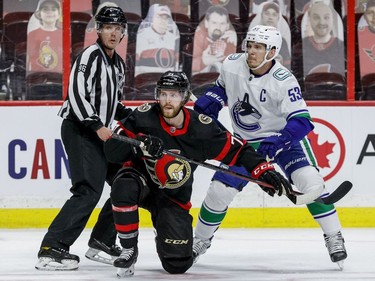 Ottawa Senators centre Chris Tierney and Vancouver Canucks centre Bo Horvat (53) get tangled up after the faceoff as linesman David Brisebois (96) looks on.