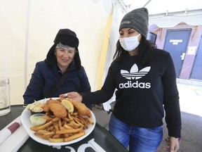 Dora Paolo serves Jo-Anne Park (left) fish and chips on Good Friday at Timothy's pub on Browns Line in Etobicoke. The province is shutting down many businesses at 12:01 a.m. Saturday morning for the next 28 days on Friday, April 2, 2021.