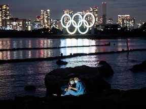 A couple pose for pictures before the lit Olympic rings at the Odaiba waterfront in Tokyo on May 6, 2021.