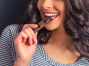 Cropped image of attractive girl eating chocolate and smiling, against dark background