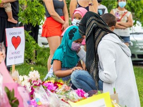 Kira Stephani speaks with her daughters Aisha Sayyed (front) and Aliyah Sayyed on Tuesday, June 8, 2021, at a makeshift memorial at the crime scene where a man driving a pickup truck jumped the curb and ran over a Muslim family in what police say was a deliberately targeted anti-Islamic hate crime in London, Ont.