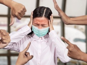 Asian woman was sick with high fever wearing hygienic mask are bullied and hate surrounded by hands mocking her, scoffing in the outbreak situation of Coronavirus 2019 infection or Covid-19