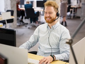 Portrait of consultant agent man in call center smiling. Happy customer support agent working with headset while sitting at his workstation. Smiling telephone operator using computer in modern open space office.