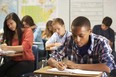 Male student in classroom writing in notebook