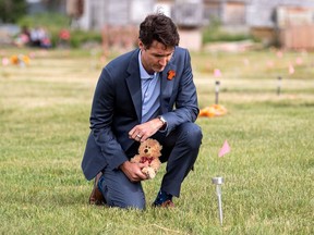 Prime Minister Justin Trudeau lays a teddy bear at a small flag in a field prior to a ceremony at the site of a former residential school where ground-penetrating radar detected a potential 751 unmarked graves, in Cowessess First Nation, Sask.