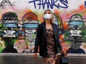 FILE: A woman wearing a face mask stands in front of graffiti.