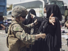 A U.S. Marine checks a woman as she goes through the Evacuation Control Center during an evacuation at Hamid Karzai International Airport in Kabul, Afghanistan, Saturday, Aug. 28, 2021.