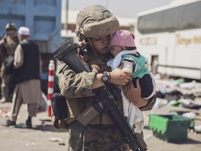 This U.S. Marine photo released Aug. 29, 2021 shows a U.S. Marine with the 24th Marine Expeditionary Unit (MEU) carrying a baby as the family processes through the Evacuation Control Center (ECC) during an evacuation at Hamid Karzai International Airport, Kabul, Afghanistan, on Aug. 28, 2021.