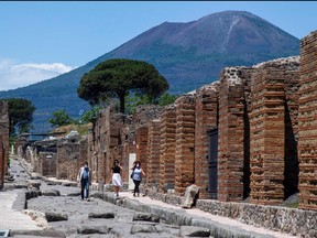 In this file photo taken on May 26, 2020, visitors walk across the archeological site of Pompeii at the bottom of the Mount Vesuvius volcano (rear), as the country eases its lockdown aimed at curbing the spread of the COVID-19 infection, caused by the novel coronavirus.