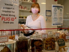 Sophie Gourves, co-owner of Mamie Clafoutis French bakery in Westboro, stands near her front counter, which is covered with plexiglass and has clear signs about vaccine passports being required for indoor dining.