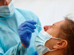 A nurse wearing a protective suit and a face mask uses a nose swab on a patient in a testing area.