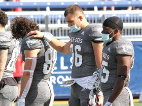 Ottawa Gee-Gees players, from left Dylan St. Pierre, Kylian Fresno and Tristin Park join in the moment of silence in memory of defensive lineman Francis Perron, who had died a week earlier following a game in Toronto.