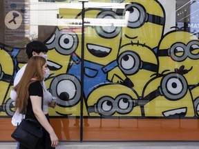FILE: Pedestrians wearing masks walk by Minions characters displayed in a window.