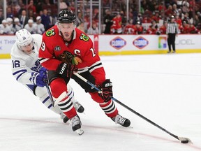 Jonathan Toews #19 of the Chicago Blackhawks turns with the puck under pressure from Mitchell Marner #16 of the Toronto Maple Leafs at the United Center on October 27, 2021 in Chicago, Illinois.