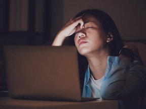 A woman working late at night, suffering burnout.