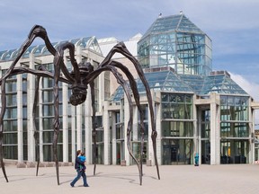 A man carries his young son underneath a spider sculpture entitled Maman in front of the National Gallery of Canada.
