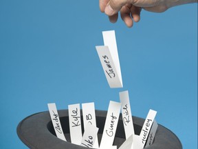 Hand throwing a piece of paper with a name on it into a hat with other names