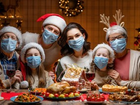 Merry Christmas! Happy family are having dinner at home. Celebration holiday and togetherness near tree. People are wearing facemasks.