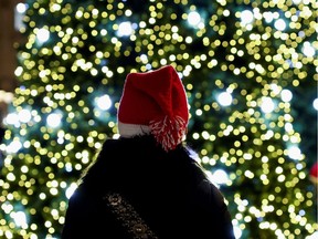 A woman with a Christmas hat stands near Christmas trees.
