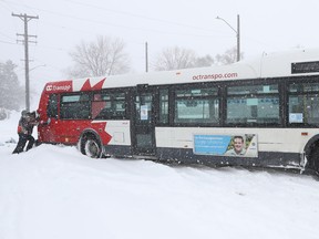 Jen Mayhew and her son Brayden try to help push out a stuck OC Transpo bus on Carleton Ave. in Ottawa Monday.