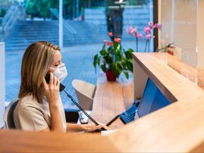 young woman answer the phone at the reception with coronavirus mask