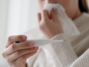 Une jeune femme asiatique malade s'assoit sous une couverture sur un canapé et éternue avec du papier de soie à la maison. Femme se moucher, tousser, éternuer, vérifier la température dans les tissus à la maison, souffrant de grippe. Concept de rhume et de fièvre