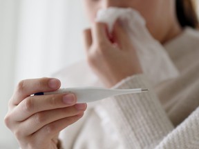 Une jeune femme asiatique malade s'assoit sous une couverture sur un canapé et éternue avec du papier de soie à la maison.  Femme se moucher, tousser, éternuer, vérifier la température dans les tissus à la maison, souffrant de grippe.  Concept de rhume et de fièvre