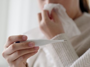 Sick young asian woman sit under blanket on sofa and sneeze with tissue paper at home. Female blow nose, coughing, sneezing, check temp in tissue at home, suffering from flu. Cold and fever concept