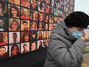 A woman cries in front of a huge screen bearing portraits of late crew members and passengers of Ukraine International Airlines Flight 752, which crashed in Iran a year before, during a commemorative ceremony on January 8, 2021 at the site of a future memorial on the Dnipro river bank in Ukraine's capital Kiev.