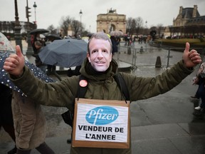 A demonstrator poses for a picture wearing a mask of French President Emmanuel Macron and a sign that reads, "Pfizer seller of the year," at a protest against a bill that would transform France's current coronavirus disease health pass into a ''vaccine pass'', in Paris, France, Jan. 8, 2022.