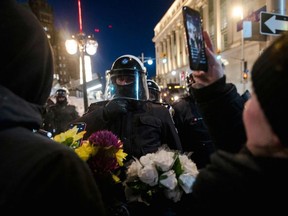A woman livestreams while handing out flowers in front of police as protesters gather and party on Kent Street after police cleared Wellington Street, previously occupied by the Freedom Convoy, in Ottawa, on February 19, 2022.
