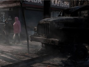People walk past a burnt vehicle as Russia's invasion of Ukraine continues in Kyiv on Feb. 28, 2022.