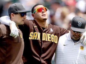 Manny Machado of the San Diego Padres is helped off the field by acting manager Ryan Flaherty and head trainer Mark Rogow after being injured trying to reach first base against the Colorado Rockies in the first inning at Coors Field on June 19, 2022 in Denver.