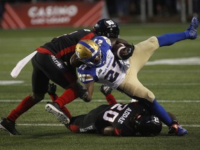 Winnipeg Blue Bombers running back Johnny Augustine is tackled by Ottawa Redblacks defensive back Monshadrik Hunter (left) and Alonzo Addae during the first half.