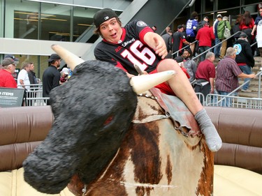 Ian Wightman gets tossed around on a mechanical bull outside the front gate before the game between the Redblacks and Blue Bombers.
