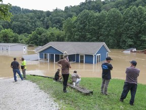 A family watches their home submerged by floodwaters from the North Fork of the Kentucky River in Jackson, Kentucky on July 28, 2022. - Flash flooding caused by torrential rains has killed at least eight people in eastern Kentucky and left some residents stranded on rooftops and in trees, the governor of the south-central US state said Thursday.