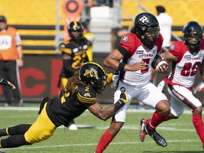 Ottawa Redblacks quarterback Caleb Evans (5) is tackled by Hamilton  Tiger Cats defensive back Tunde Adeleke (2) during first half CFL  football game action in Hamilton, Ont. on Saturday, July 16, 2022.