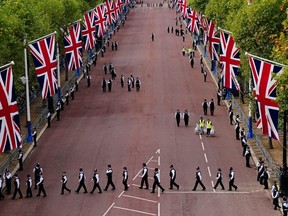 Police officers take up positions as street workers clear away rubbish along The Mall ahead of the ceremonial procession of the coffin of Queen Elizabeth II from Buckingham Palace to Westminster Hall, London, Wednesday Sept. 14, 2022.