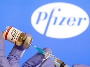 A woman holds a small bottle labelled with a "Coronavirus COVID-19 Vaccine" sticker and a medical syringe in front of displayed Pfizer logo in this illustration taken Oct. 30, 2020.