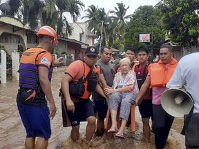 In this image provided by the Philippine Coast Guard, an elderly woman sits on a chair while being carried by coast guard personnel wading through floodwaters in Plaridel, Misamis Occidental province in the southern Philippines, Monday, Dec. 26, 2022.