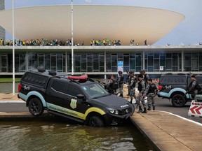 In this file photo taken on Jan. 8, 2023, members of the Federal Legislative Police stand next a vehicle that crashed into a fountain as supporters of Brazilian former President Jair Bolsonaro invade the National Congress in Brasilia.