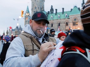 File photo/ Pat King, one of the organizers of the "Freedom Convoy", signs a flag in front of Parliament Hill, Feb. 16, 2022.