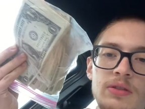 Young man holding up plastic bag filled with money.