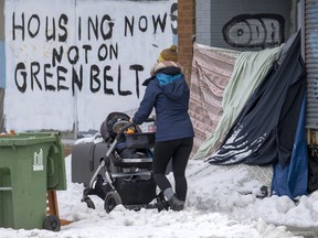A woman pushes a stroller past the shelter of an unhoused person in Toronto on Tuesday January 31, 2023 as the coldest weather in years arrives.