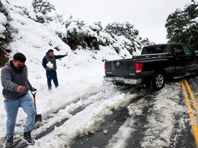People assist the driver of a truck which became stuck in the snow on a roadway in in Los Angeles County, in the Sierra Pelona Mountains, Saturday, Feb. 25, 2023 in Green Valley, Calif.