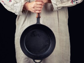 woman in a gray linen dress holds with two hands a round cast-iron pan