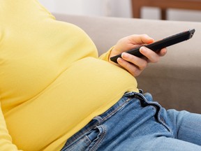 Side view of young obese woman relaxing on sofa and watching TV.