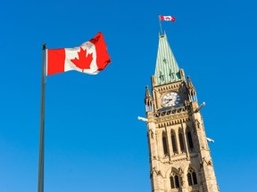 Close up of peace tower (parliament building) with a big canadian flag over blue sky in Ottawa.