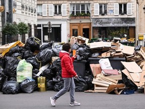 A pedestrian walks past household waste containers in Paris, Sunday, March 12, 2023, which have been piling up since collectors went on strike against the French government's proposed pension reforms a week earlier.